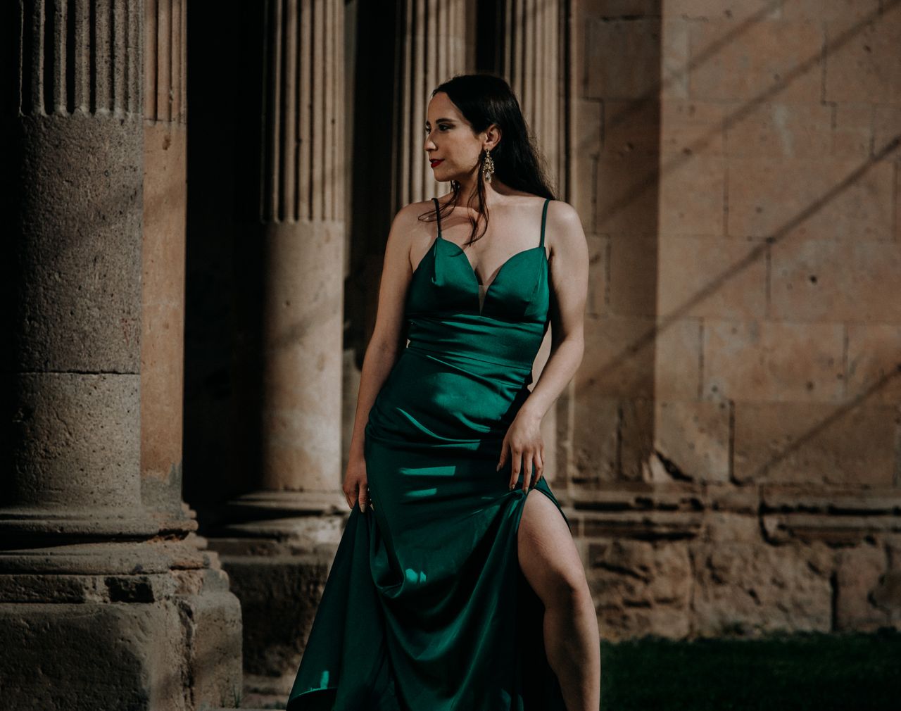 Services-01 Model in a green dress standing elegantly by ancient stone columns, exuding sophistication.