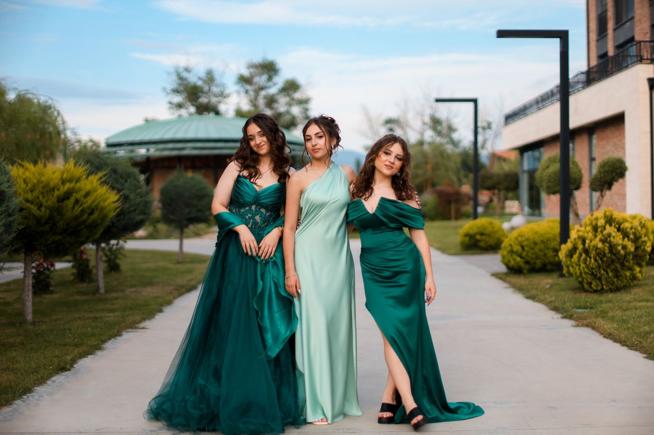 creative-03 Three women in elegant green dresses standing on a sidewalk in an urban outdoor setting.