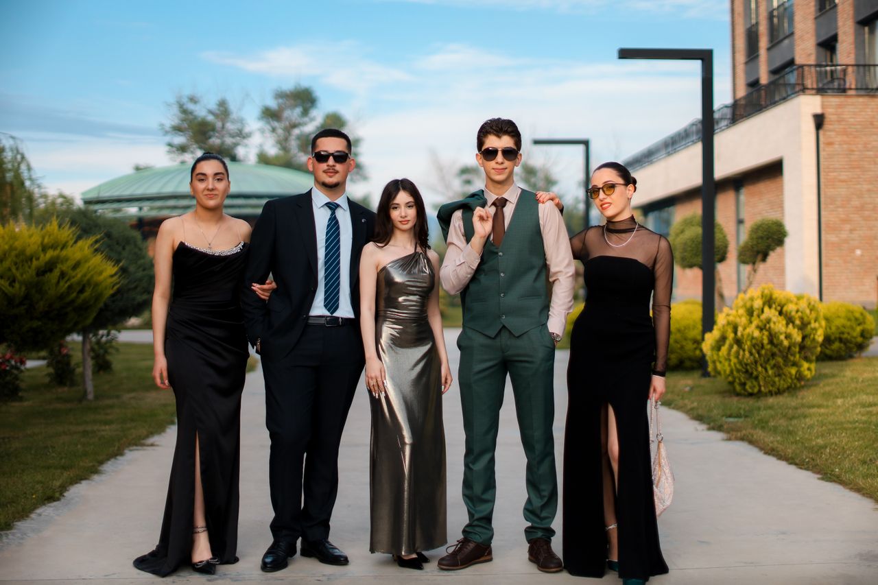 mobile-01 A stylish group of five adults in formal attire posing outdoors on a sunny day.
