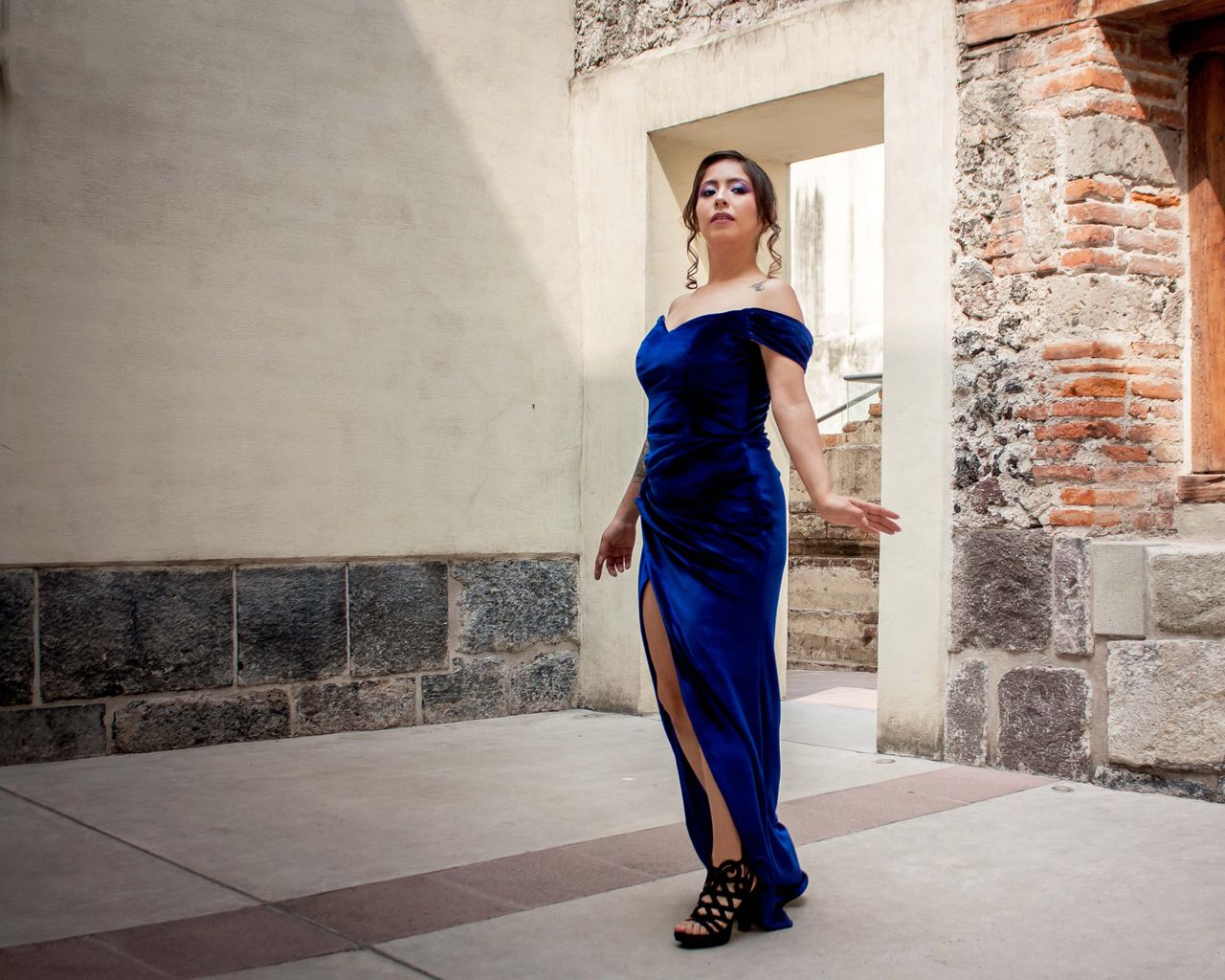 Services-03 Graceful woman in a blue dress poses against rustic architecture, showcasing elegance and style.
